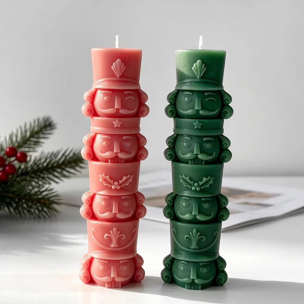 Two tall stacked nutcracker soldier candles in coral pink and deep green with raised hats, faces and uniform details