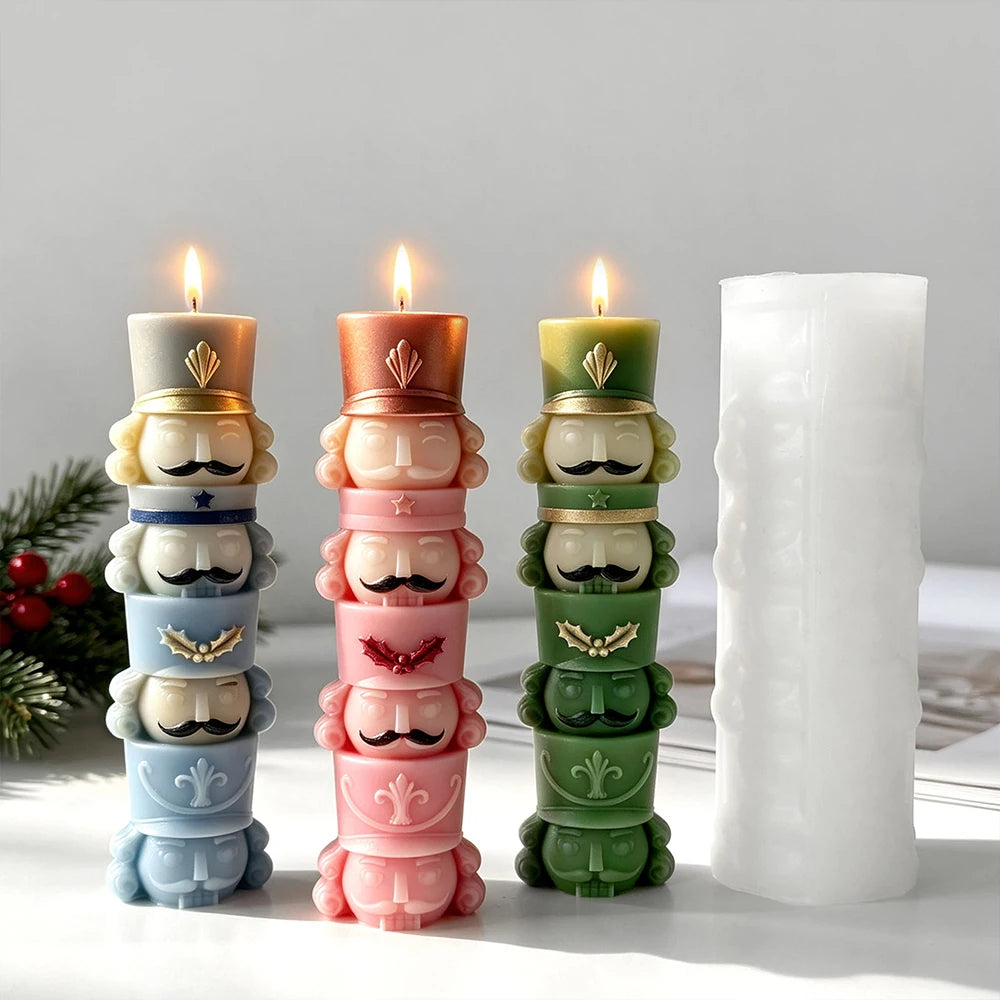 Three lit stacked nutcracker soldier candles in blue, coral pink and green beside a tall white silicone mold